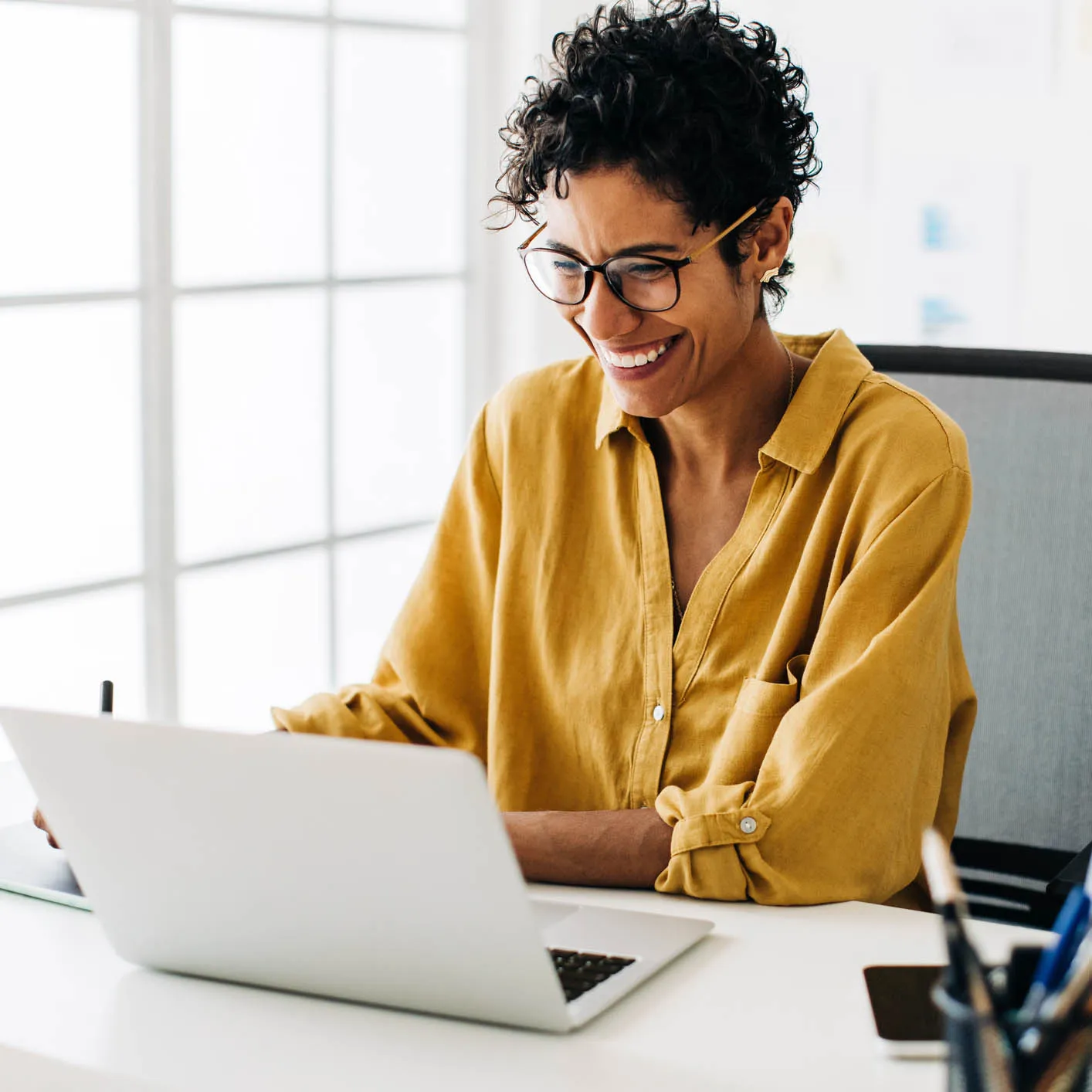 Young woman smiles at a laptop while sitting at a desk in her office
